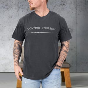 May include: Dark gray V-neck t-shirt with the text "CONTROL YOURSELF" in white, above a white horizontal line. The shirt is made of a soft material and has short sleeves.