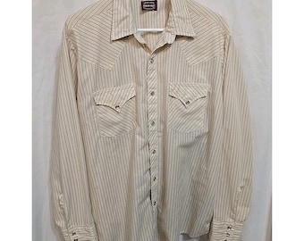 Puede incluir: Camisa abotonada de manga larga color crema con finas rayas verticales. Cuenta con dos bolsillos en el pecho con costuras decorativas y cierres a presión. La camisa tiene un estilo occidental clásico con cuello puntiagudo y puños abotonados.