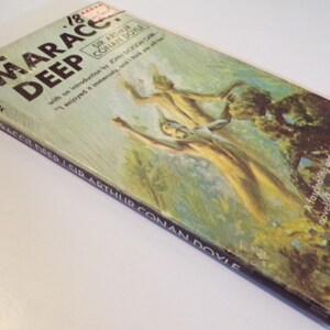 May include: A vintage paperback book cover with a green and brown illustration of a woman in a flowing white dress standing in a forest. The book title is "The Maracot Deep" by Sir Arthur Conan Doyle.