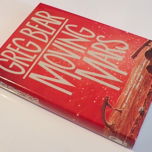 May include: A red hardcover book with the title "Moving Mars" by Greg Bear. The cover features a red and brown illustration of a Martian landscape with a large structure in the foreground.