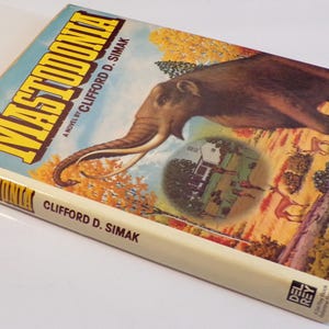 May include: A vintage paperback book titled "Mastodonka" by Clifford D. Simak. The cover features a colorful illustration of a mammoth in a forest setting with a small house in the background.