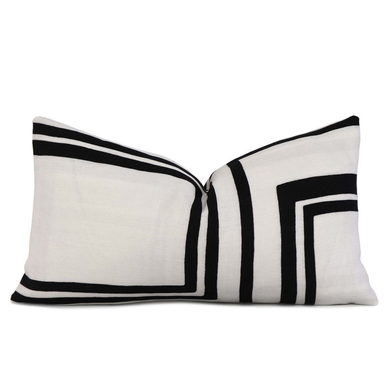 May include: A white rectangular cushion with black geometric stripes. The cushion has a simple design with a modern aesthetic.
