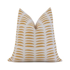May include: A decorative pillow with a white background and a repeating pattern of horizontal, golden-yellow, curved lines. The pillow is a square shape and appears to be made of a soft fabric. The design is modern and minimalist.