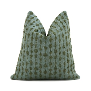 May include: A decorative pillow with a textured, woven design. The pillow features a light teal background with a pattern of raised, olive green diamond shapes. The pillow is a soft, inviting accent for any living space.