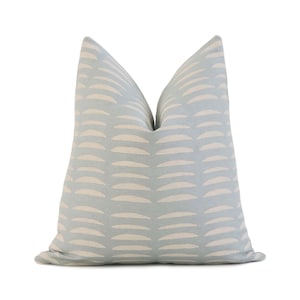 May include: A square decorative pillow with a light blue background and a repeating pattern of off-white, curved shapes. The pillow has a soft, textured appearance and is designed for home decor.