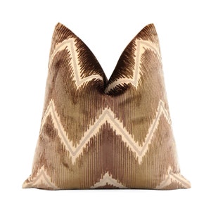 May include: A brown and beige patterned throw pillow with a chevron design. The pillow is made of a soft, velvety fabric.