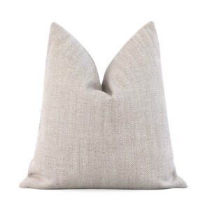 May include: A beige throw pillow with a subtle textured pattern. The pillow is made of a soft, woven fabric and has a square shape.