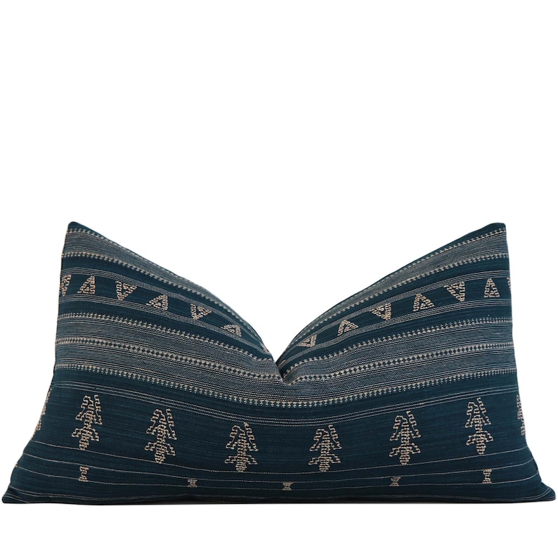 Puede incluir: Coj&iacute;n de tiro azul teal con un patr&oacute;n geom&eacute;trico de tri&aacute;ngulos y rayas en un tono de azul m&aacute;s claro. El coj&iacute;n tiene un patr&oacute;n repetitivo de &aacute;rboles estilizados en color beige.