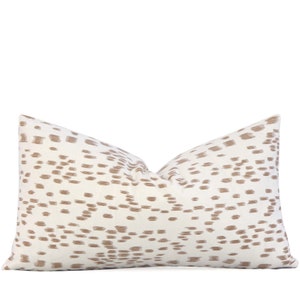 May include: A white pillow with a brown abstract pattern. The pattern is made up of small, irregular shapes that resemble dots or dashes.