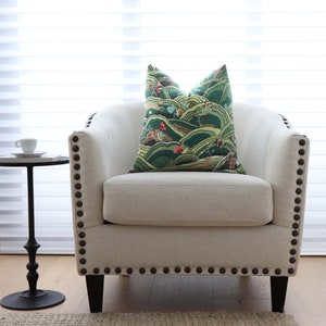 May include: A white upholstered armchair with a green and brown patterned pillow. The armchair has a curved back and a tufted seat. The armchair is accented with dark brown nailhead trim.