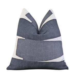 May include: A decorative throw pillow with a geometric design. The pillow features a dark gray background with white abstract shapes. The pillow is made of a textured fabric and is designed for home decor.