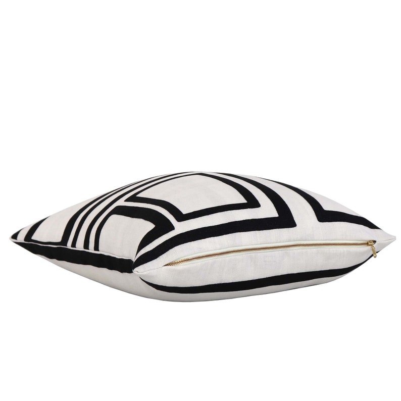 May include: White cushion with a black geometric pattern. The cushion has a zipper closure.