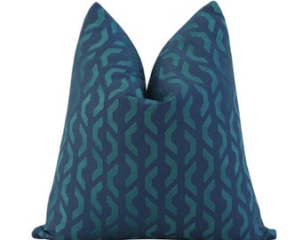 May include: A decorative throw pillow with a geometric pattern. The pillow features a dark blue background with a teal-colored interlocking design. The pillow is a square shape and is made of a soft fabric.