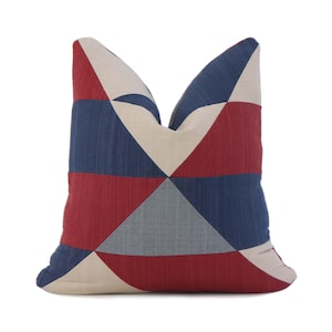 May include: Square decorative pillow with a geometric pattern in red, navy blue, light gray, and beige. The pillow features a patchwork design with triangular shapes, adding a modern touch to home decor.