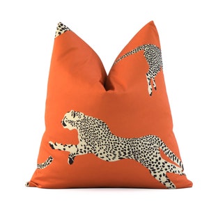 May include: Orange throw pillow with a cheetah print design. The pillow features a cheetah running across the front of the pillow.