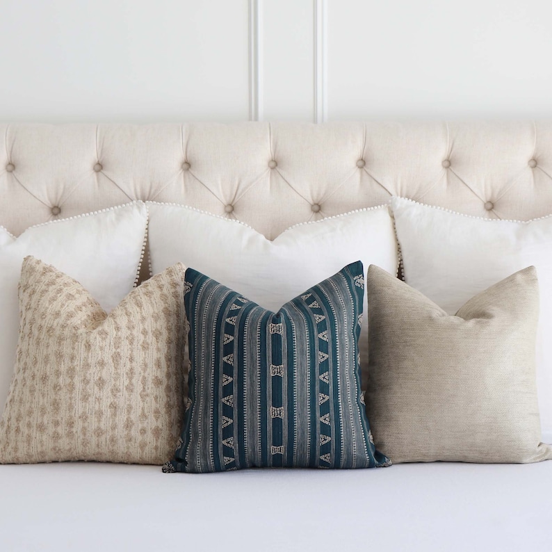 Puede incluir: Un conjunto de almohadas decorativas con una variedad de patrones y colores. Las almohadas est&aacute;n dispuestas en una cama blanca con una cabecera capiton&eacute;. Las almohadas incluyen una almohada turquesa con un patr&oacute;n geom&eacute;trico, una almohada beige con un patr&oacute;n floral y dos almohadas blancas con un ribete de cuentas.