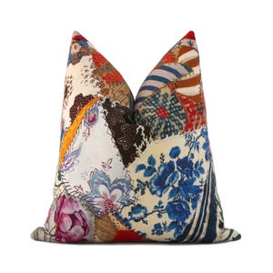 May include: A square throw pillow featuring a patchwork design of various fabric patterns including blue floral prints, red and white stripes, dark brown lace-like textures, and a large pink peony motif on a cream-colored background.