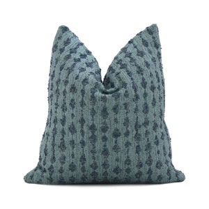 May include: A teal blue throw pillow with a textured, woven design. The pillow has a subtle geometric pattern and a soft, plush feel.