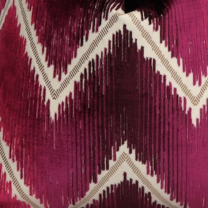 May include: Close-up of a decorative pillow with a geometric pattern. The design features a series of vertical lines in shades of burgundy and magenta, set against a cream-colored background. The lines create a zig-zag pattern.