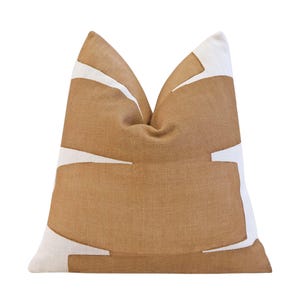 May include: A decorative pillow with a tan background and white geometric shapes. The pillow has a textured appearance and a soft, inviting look. The design is modern and would complement a variety of home decor styles.