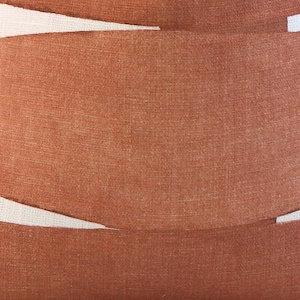 May include: Close-up of a textured, rust-colored fabric with a woven appearance. The fabric is arranged in curved bands, with white spaces between them. The overall effect is a layered, abstract design.