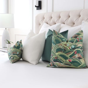 May include: A bed with a white headboard and white bedding. There are four pillows on the bed, two with a green and brown landscape pattern, one white, and one green.