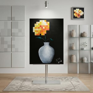 Könnte beinhalten: Ein Gemälde einer gelb-orangen, pixeligen Blume in einer weißen Vase vor schwarzem Hintergrund. Das Kunstwerk wird auf einem silbernen Ständer ausgestellt. Ein kleineres gerahmtes Stück mit ähnlichem Design hängt an der Wand.