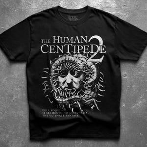 Puede incluir: Una camiseta negra de manga corta con un gráfico blanco de un rostro humano rodeado por un ciempiés. El texto dice THE HUMAN CENTIPEDE 2, FULL SEQUENCE. 12 SEGMENTS. NO ANESTHESIA. THE ULTIMATE FANTASY. La camiseta tiene un cuello redondo.