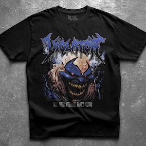 Peut inclure: T-shirt noir avec un motif de monstre bleu et marron et le mot "VIOLATOR" en bleu, texte stylisé. Le texte "NOT YOUR AVERAGE PARTY CLOWN" est en dessous du motif. Le t-shirt a un col rond.