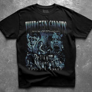 May include: A black short-sleeve t-shirt featuring a graphic print with the text THIR13EN GHOSTS and MISERY LOVES COMPANY. The design includes blue-toned illustrations of multiple ghostly figures and faces, along with a row of symbols at the bottom.