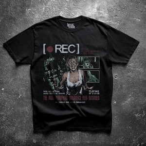 Puede incluir: Camiseta negra con un gráfico de la película de terror "REC". El diseño incluye la palabra "REC" con un círculo rojo, imágenes de la película y el texto "The Most Terrifying Experience Ever Recorded."