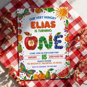 以下が含まれることがあります： 「Our Very Hungry Elias is Turning One」のテキストが入ったカラフルな招待状。デザインには、果物、イモムシ、笑顔の太陽、蝶のイラストが含まれています。招待状には、イベントの日付、時間、場所も含まれています。