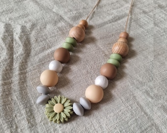 May include: A necklace with a variety of beads in shades of brown, white, green, and gray. The necklace features wooden beads, round beads, and a green flower-shaped pendant. The necklace is strung on a natural-colored cord.