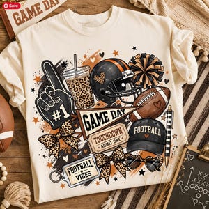 May include: A cream-colored t-shirt featuring a graphic print of football-themed items including a helmet, a football, a foam finger with #1, a pennant reading GAME DAY, a ticket reading TOUCHDOWN ADMIT ONE, and a tag reading FOOTBALL VIBES.