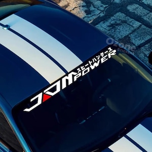 May include: A blue car bonnet with white racing stripes and a windscreen sticker. The sticker features the text "JDM POWER" in white block letters with a red triangle accent, and Japanese characters. The sticker also has the text "Ozone Stickers".
