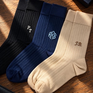 May include: Three pairs of ribbed crew socks in black, navy blue, and beige. The black pair features white embroidered initials PT, the navy pair has light blue embroidered initials RRB, and the beige pair has brown embroidered initials J.B.