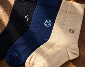 May include: Three pairs of ribbed crew socks in black, navy blue, and beige. The black pair features white embroidered initials PT, the navy pair has light blue embroidered initials RRB, and the beige pair has brown embroidered initials J.B.