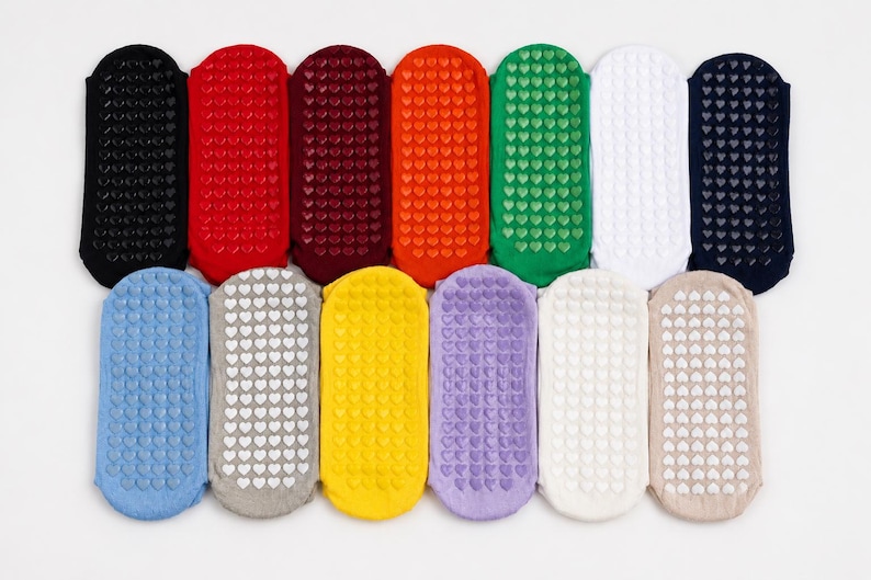 May include: A collection of thirteen low-cut ankle socks arranged in two rows, featuring a variety of solid colors including black, red, maroon, orange, green, white, navy, blue, gray, yellow, purple, cream, and beige with heart-shaped grips.