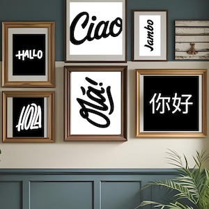 May include: A selection of framed art prints with greetings in different languages. The prints have bold, white text on black and white backgrounds. The frames are in shades of brown and gold, creating a decorative wall display.