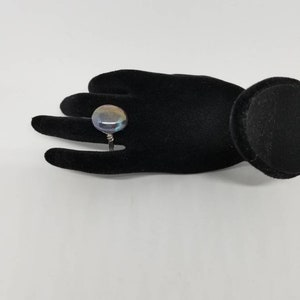 Puede incluir: Un anillo de plata con una gran piedra preciosa redonda e iridiscente. La piedra preciosa tiene tonos de azul, verde y morado.
