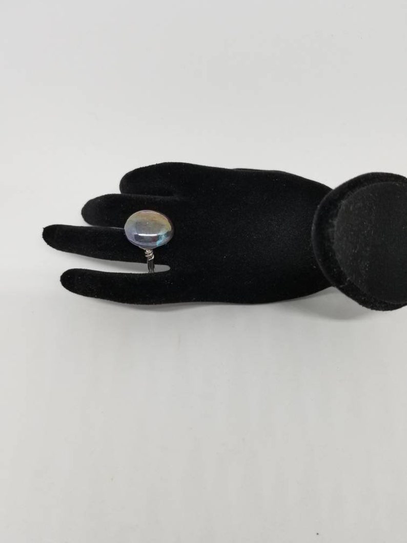 Puede incluir: Un anillo de plata con una gran piedra preciosa redonda e iridiscente. La piedra preciosa tiene tonos de azul, verde y morado.
