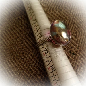 Puede incluir: Un anillo de plata con una piedra de vidrio grande, iridiscente y multicolor. El anillo est&aacute; dimensionado en un calibrador de anillos de metal marcado con los n&uacute;meros 16 a 20.