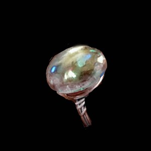 Puede incluir: Un anillo de vidrio transparente con una banda plateada. El vidrio tiene un acabado iridiscente con tonos de azul, verde y dorado.