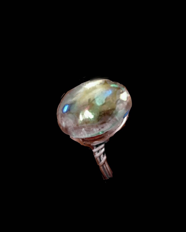 Puede incluir: Un anillo de vidrio transparente con una banda plateada. El vidrio tiene un acabado iridiscente con tonos de azul, verde y dorado.