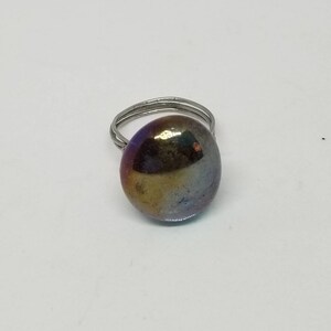 Puede incluir: Un anillo de plata con una gran piedra ovalada iridiscente. La piedra tiene tonos de morado, azul, verde y dorado.