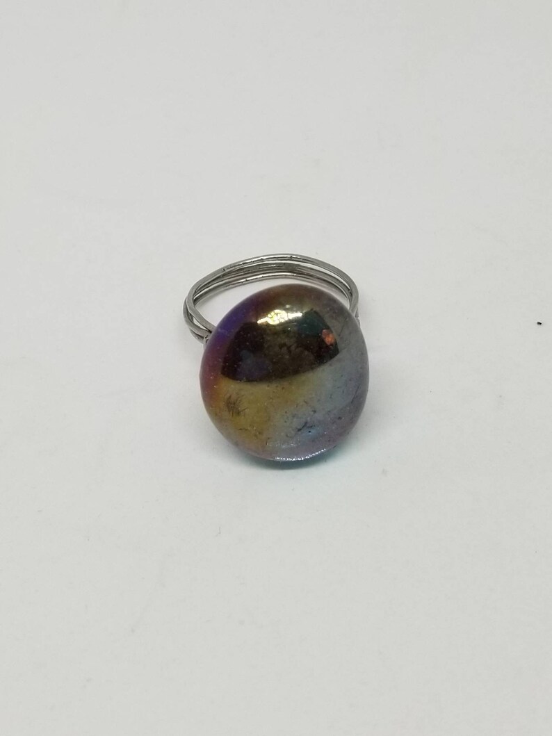Puede incluir: Un anillo de plata con una gran piedra ovalada iridiscente. La piedra tiene tonos de morado, azul, verde y dorado.