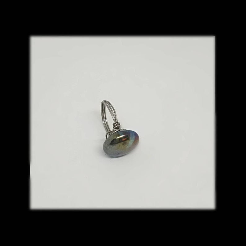 Puede incluir: Un anillo de alambre plateado con una piedra ovalada de color iridiscente oscuro.