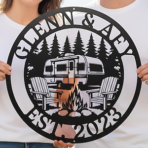 May include: A black metal sign with a camping theme. The sign features a camper, Adirondack chairs, a campfire, and the text "GLENN & AFY EST 2023". The sign is round and held by two people.