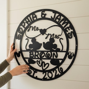 May include: Black metal wall art featuring the names "Sophia & James" and "Broom" in a circular design. Includes Mickey and Minnie Mouse silhouettes, hearts, and the year "2020". Ideal for a wedding or anniversary celebration.