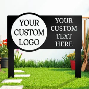 May include: Black metal garden sign with a white circle for a custom logo and space for custom text. The sign is in a grassy garden with flowers and stepping stones.